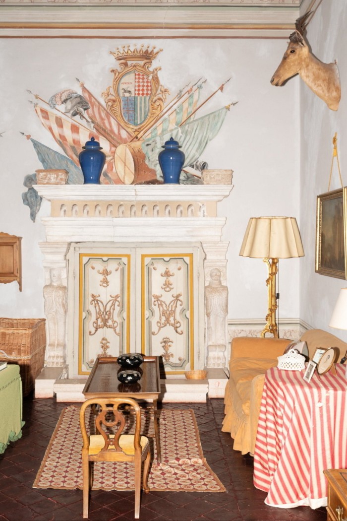 The interior of a historic Italian palazzo, with an ornately decorated stove, a sofa and a trophy head of deer