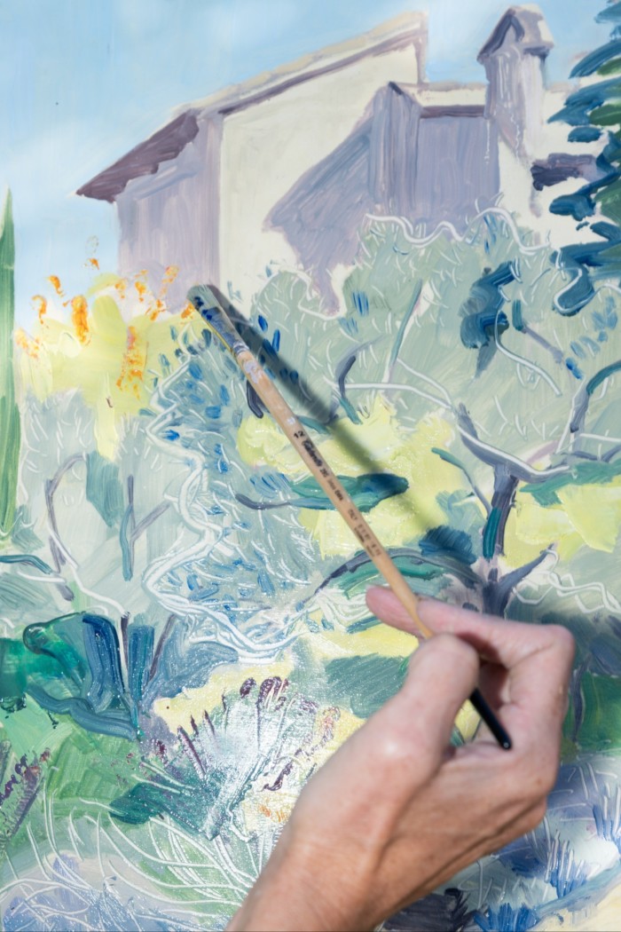 A close-up of the canvas, with a hand using a paintbrush to paint leaves on trees