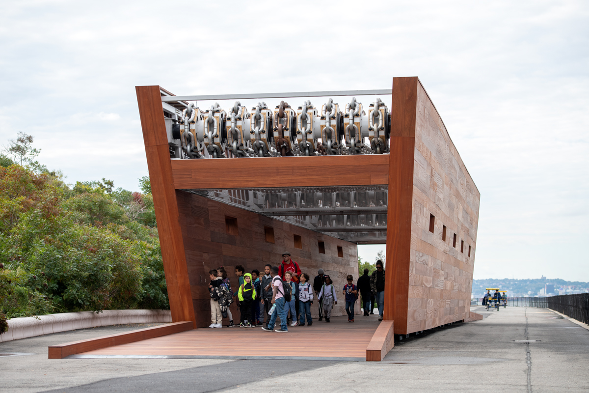 A monumental wooden sculpture that resembles a ship, showing people walking through it. 