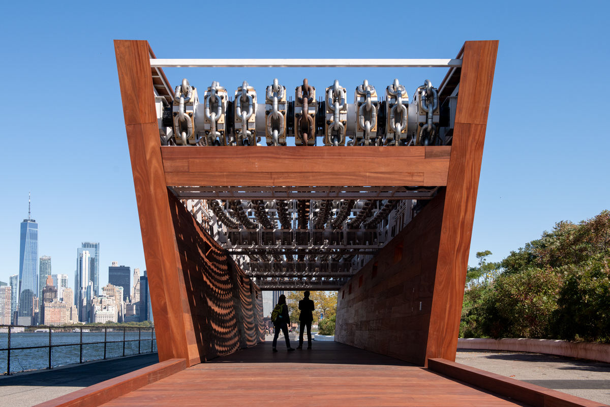 A monumental wooden sculpture that resembles a ship, showing people walking through it. 
