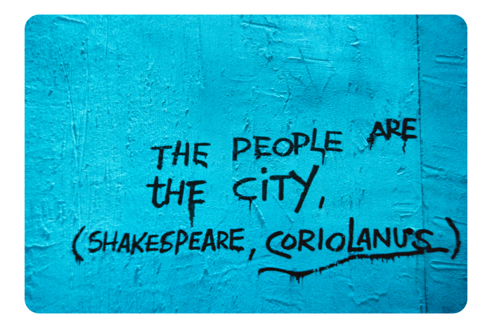 A photograph of a bright blue paper sign.The words: ‘The people are the city’ (Shakespeare, Coriolanus)’ are written on it in black capital letters