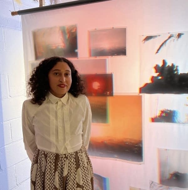 The artist stands in front of a sheet with photographs.