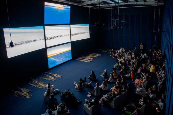 An audience watch four screens in the shape of a cross which feature both a frozen landscape and a desert where hundreds of wild horses gallop in a straight line