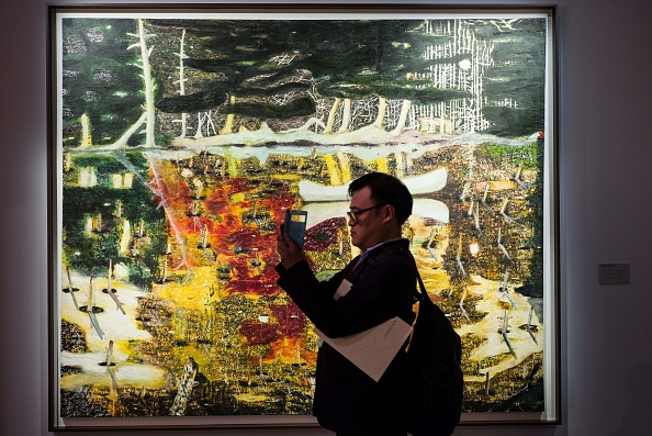 A man holds a phone in front of a colorful painting