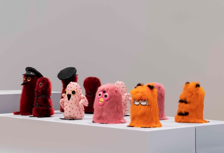 Photo of eight furry sculptures arranged on a white plinth in a white wall gallery. They're all variations on Ookpiks, furry owl characters.