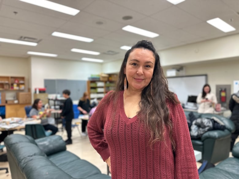  A woman in a cranberry-coloured sweater stands to have her portrait taken. In the background there are children doing art.