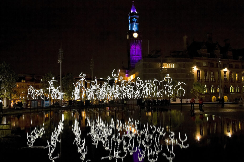 Stick figure sculptures glow white against the night sky in Bradford city centre 