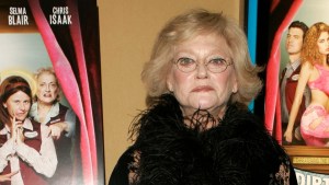 An older women with light-toned skin looks at the camera, surrounded by movie posters.