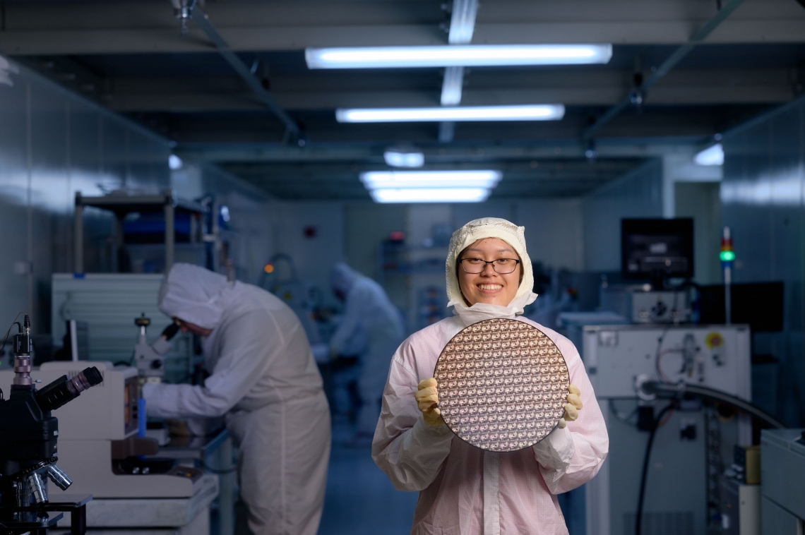a person in a lab suit holding a test wafer while standing in a lab
