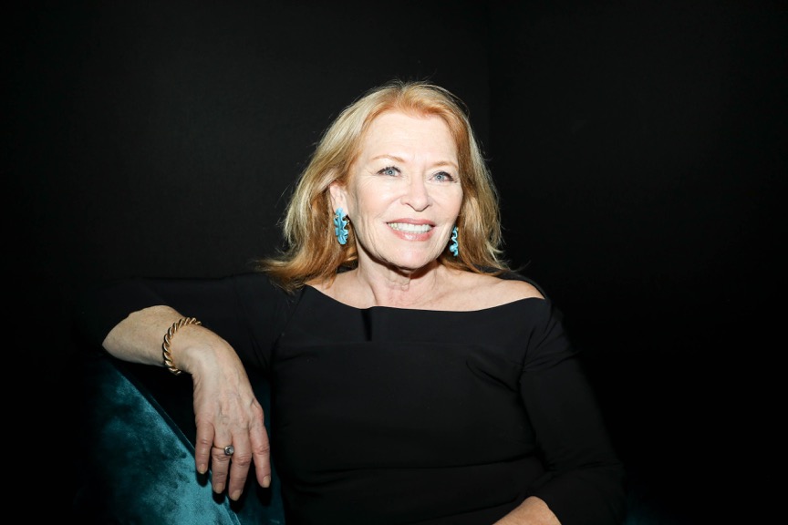 A portrait of a woman with blond hair wearing black paired with teal earrings