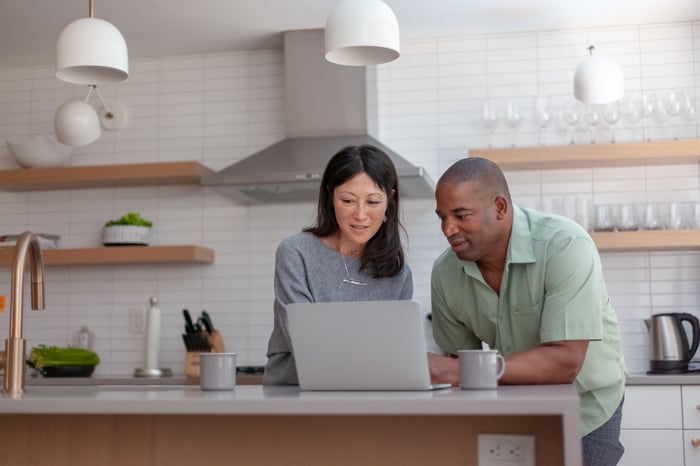 A couple in their kitchen looking at a laptop computer while they do retirement planning together.