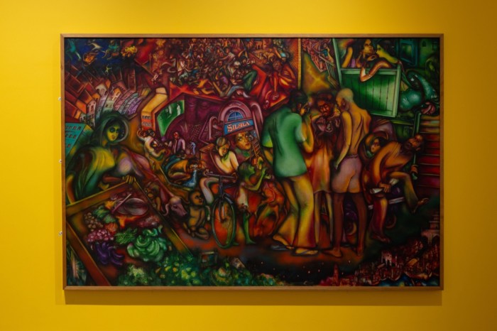 A colourful oil painting where people in an urban setting are squeezed together amid a melee of houses, animals and activity