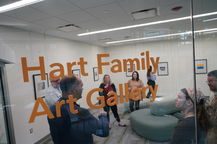 People mingle behind a glass wall that has Hart Family Art Gallery on it