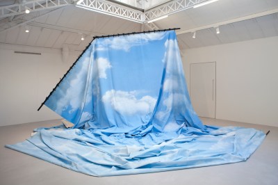 A hanging photo backdrop showing a cloudy sky. The backdrop is bent, and much of it spills onto a gallery floor.