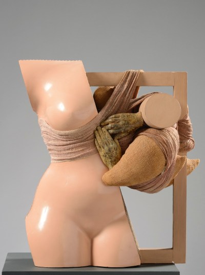 A sculpted half of a woman's nude body with a tied form intertwined with a frame.