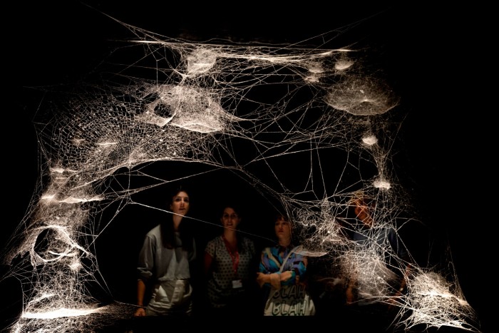 Visitors to a gallery stand in front of a spider-web-like art installation