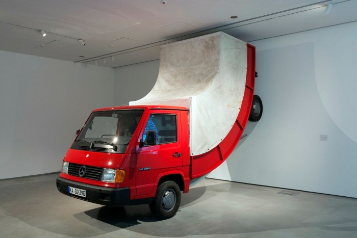 Imaging a red truck backing into a wall but instead of crumpling, it is bending up the wall
