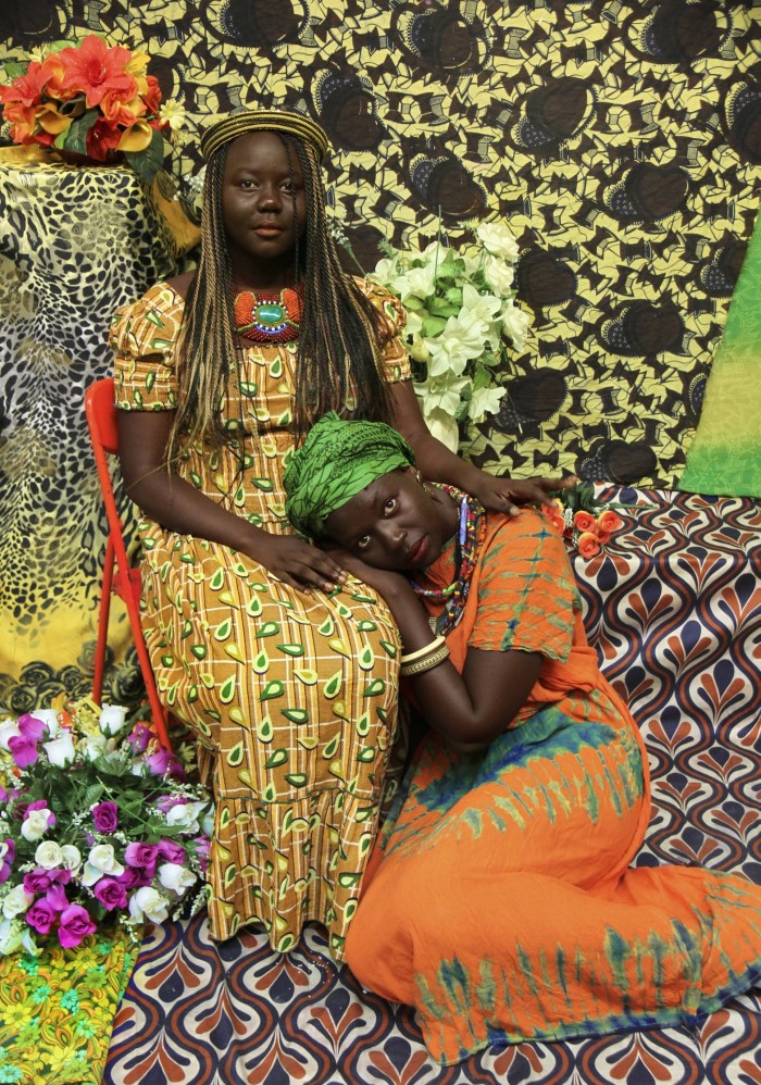 Photo of two women in bright African-print dresses against a bright African-print backdrop