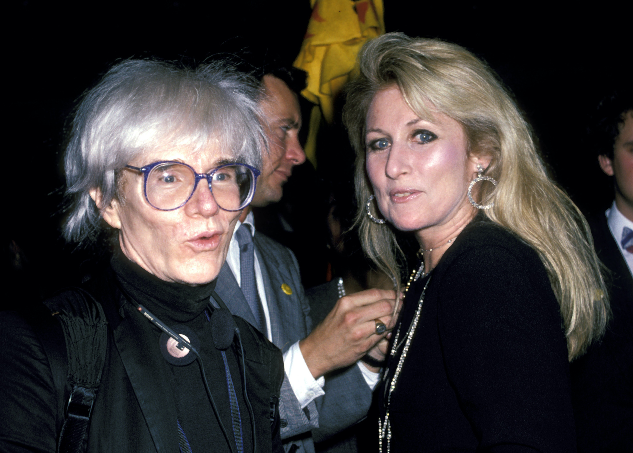 Andy Warhol standing next to young woman with long blonde hair.