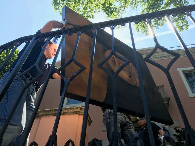 SAMFA board member Jeff Curry helps carry a large painting by San Angelo artist René Alvarado into the European Union residence on May 15, 2019.
