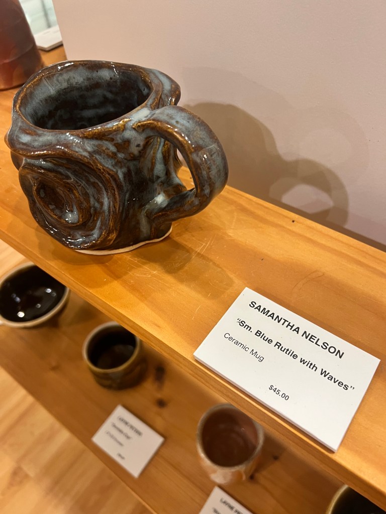 A ceramic mug titled "Blue Rutile with Waves" on display at Racine's Artists Gallery.