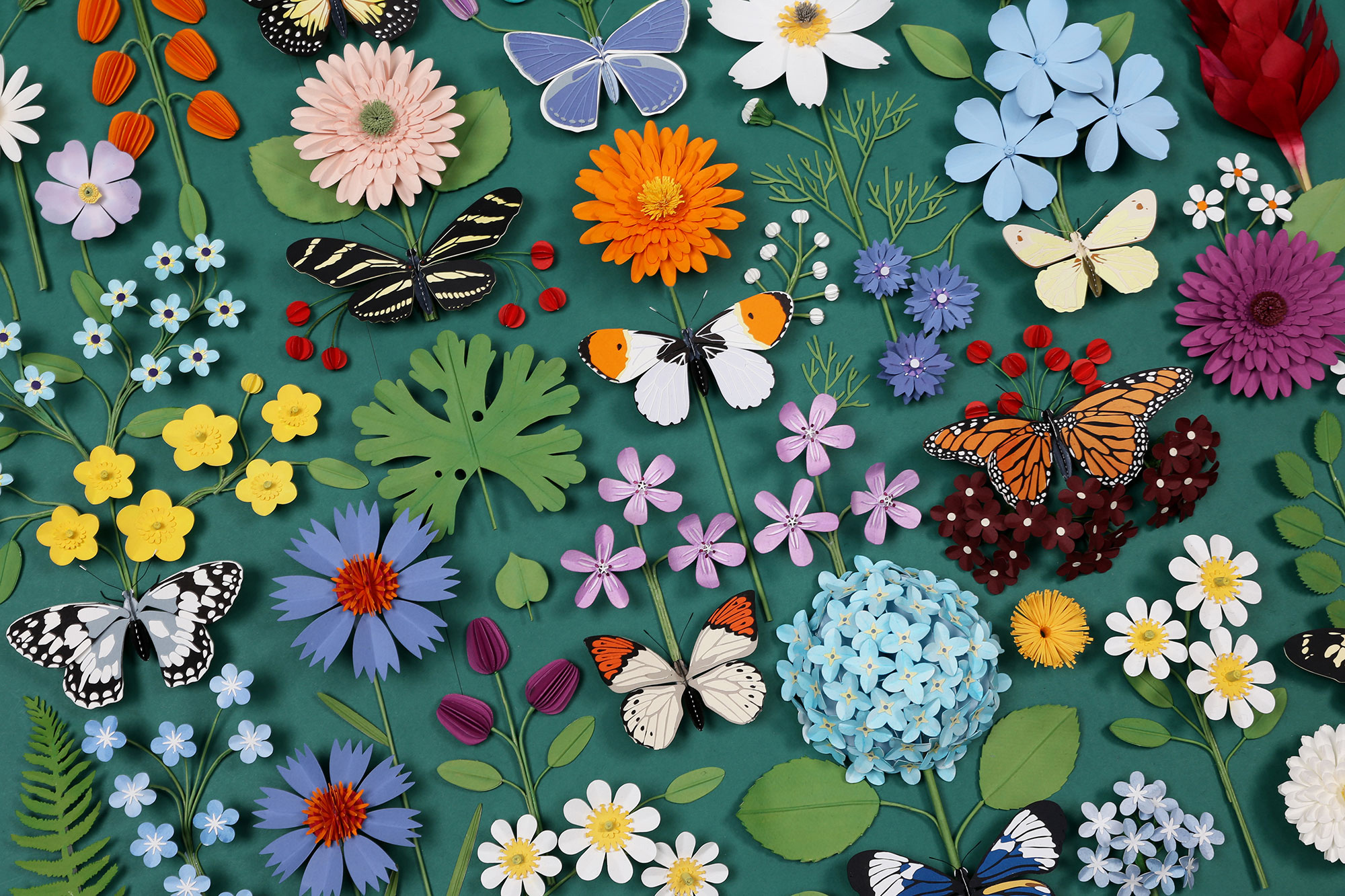 a flat lay of paper flowers and butterflies on a green backdrop