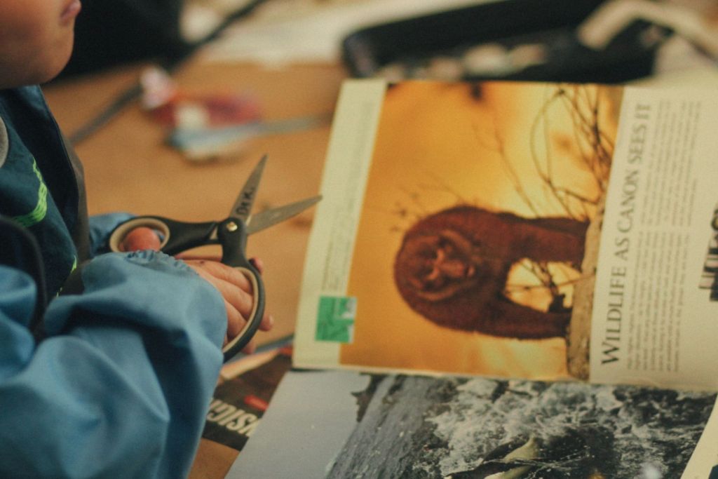 A person holds a pair of scissors next to magazines.