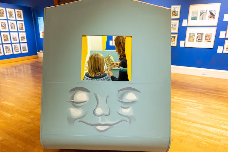 A child and parent reading in a cubicle with a face.