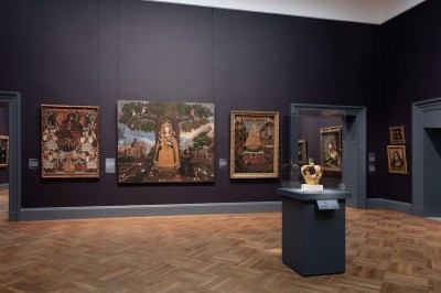 A golden crown on a pedestal in the center of a gallery of religious paintings.