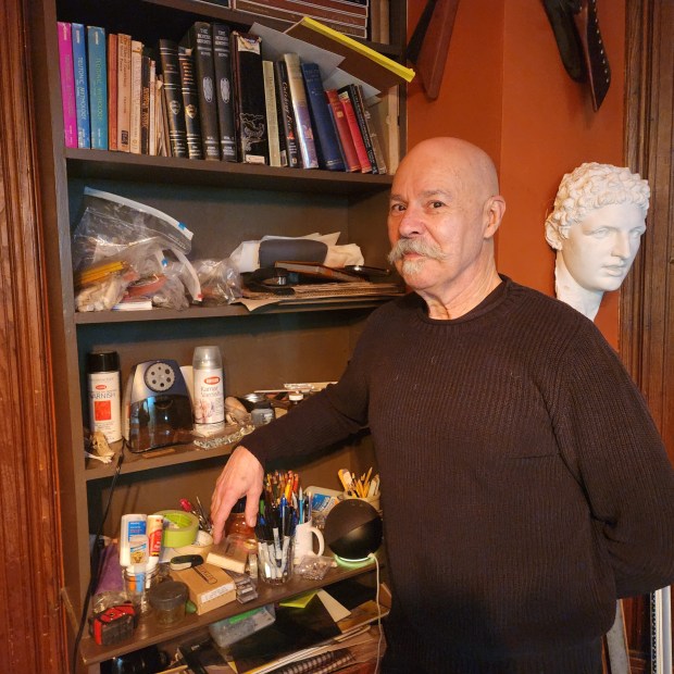 Bald man with moustache standing in front of book shelf.