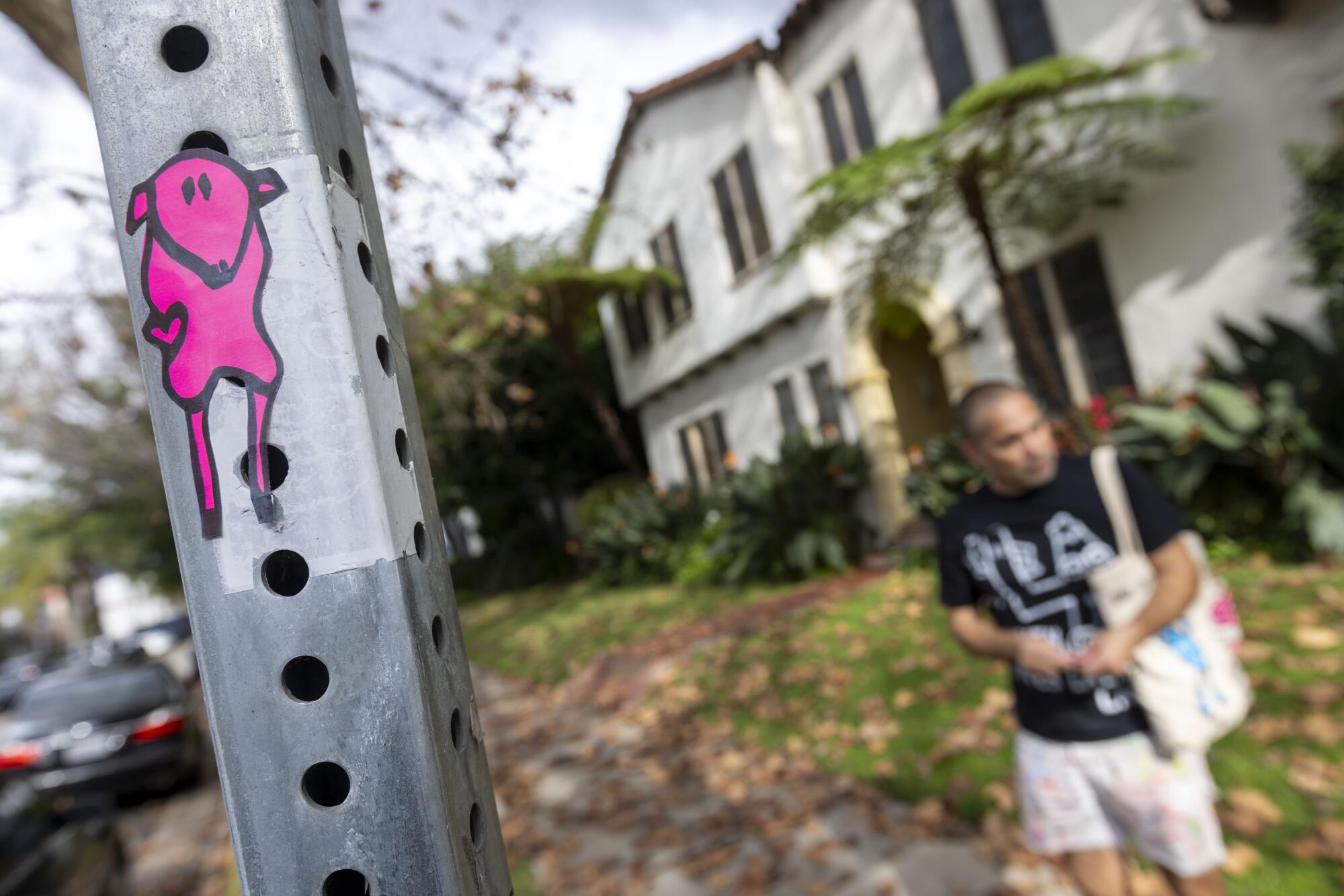 A man stands behind a post that has a pink cartoon sheep pasted on it. 