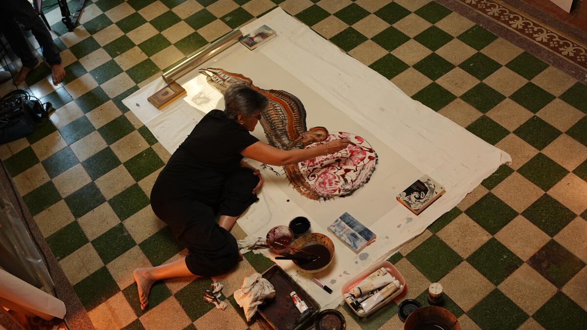 A woman paints a canvas laying on the floor.