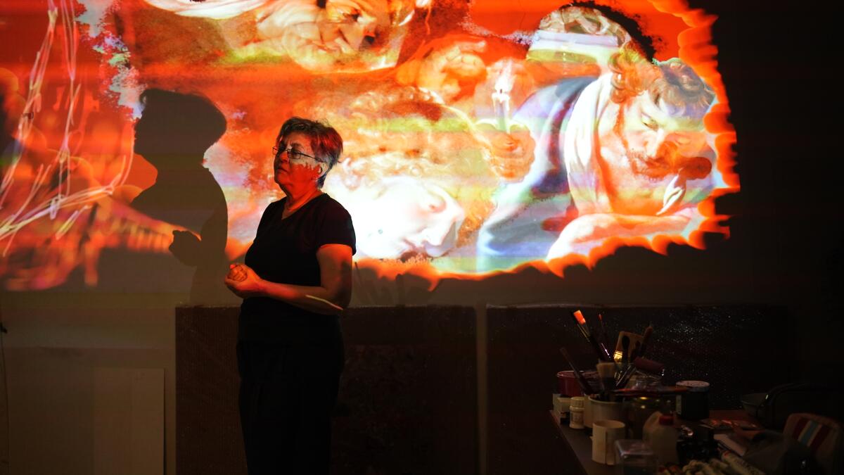 A woman stands in a room and colored projections play over her face and body.