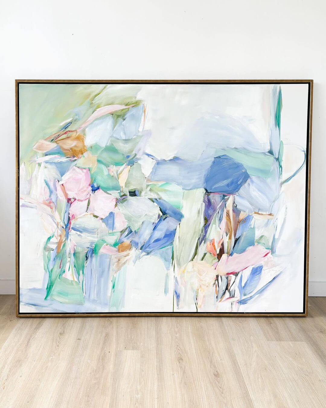 Abstract painting with pastel colors displayed on a wooden floor against a white wall.