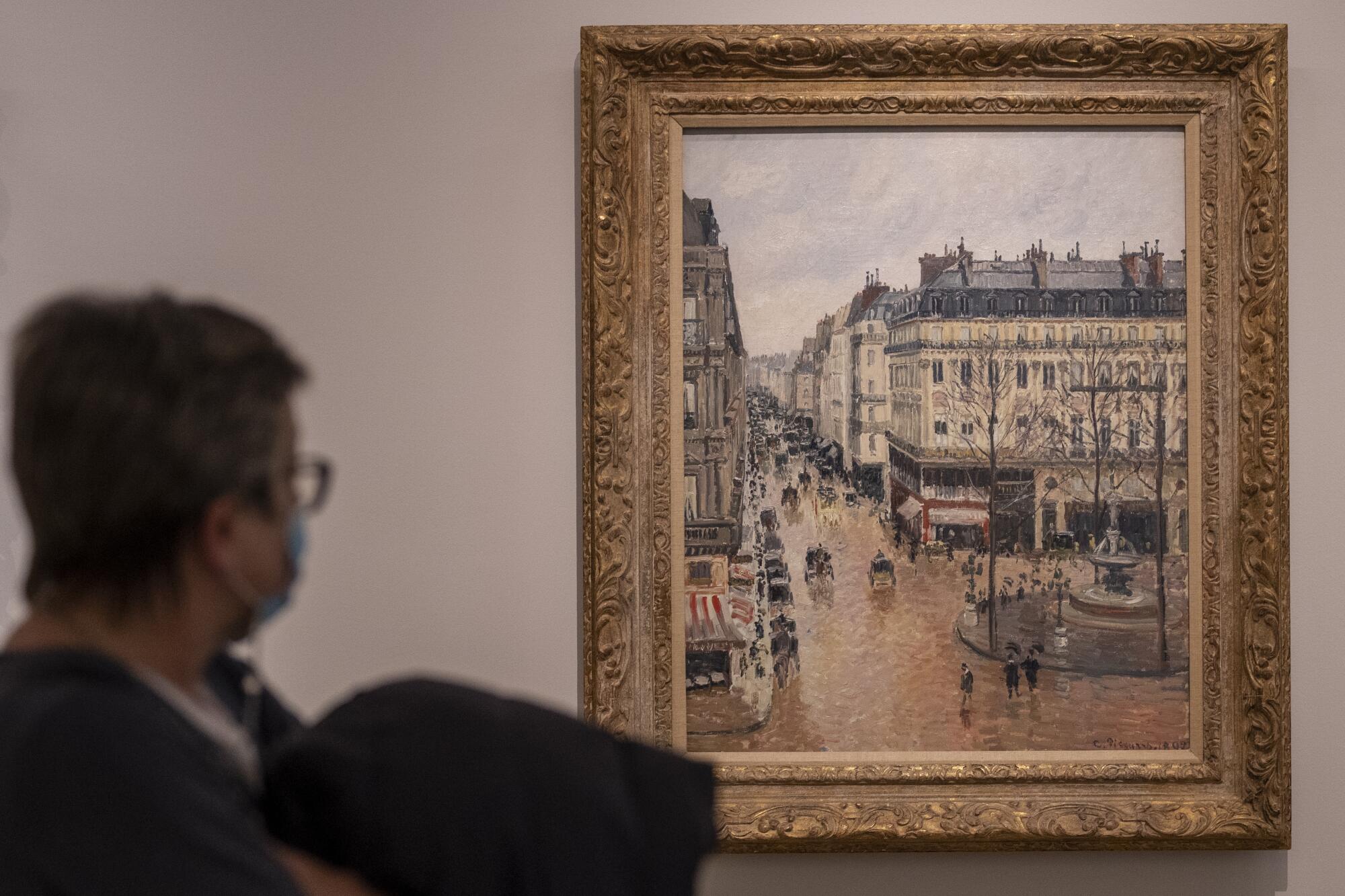 A woman looks at the Impressionist painting called "Rue St.-Honore, Apres-Midi, Effet de Pluie" 