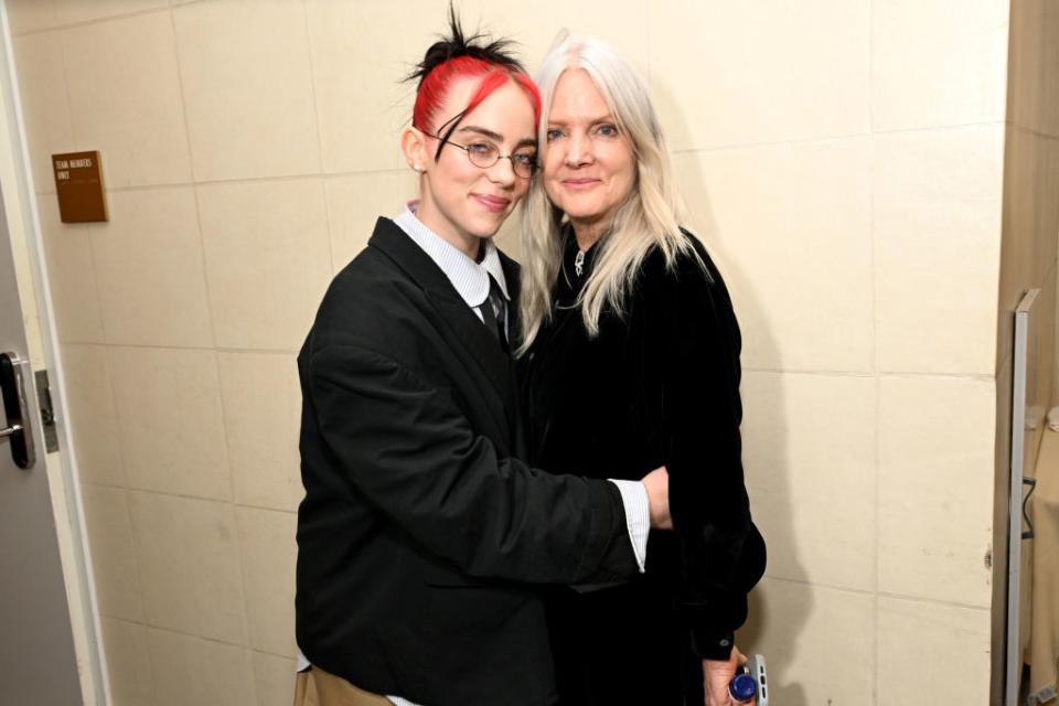 Two people standing close, one with red streak in hair, other with white hair, both in black attire