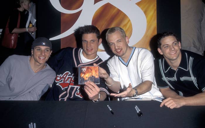 Four members of a music group sitting at a signing table with a promo card