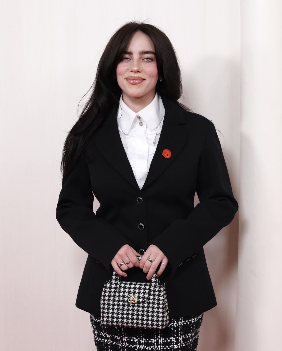 Billie Eilish in a black blazer, white shirt, holding a checkered handbag
