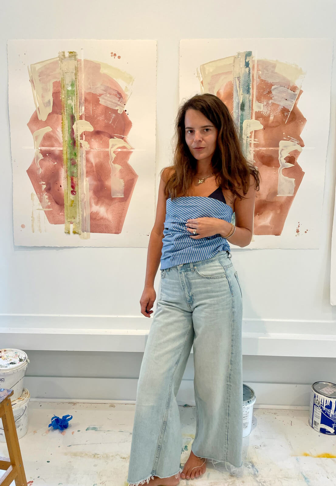 Laura Deems in her art studio in front of two abstract paintings displayed behind her.