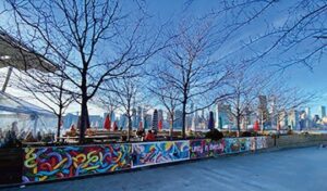 Frank Ottomanelli has just released a second Request For Proposals (RFP) for the community mural at Ottomanelli’s By The Water. He’s already installed five sections, and now he’s looking for more art as he builds a roughly 11,000-square-foot, three-foot-high panorama that’ll wrap around his concession’s outside dining area in Hunter’s Point Park South. Talisa Almonte, Kerri Boccard, Adela Navarro, Victoria Nieto, and Annabelle Popa were the first-round winners. Their pieces were installed during a ceremony on Dec. 16, 2023, and are still on display.