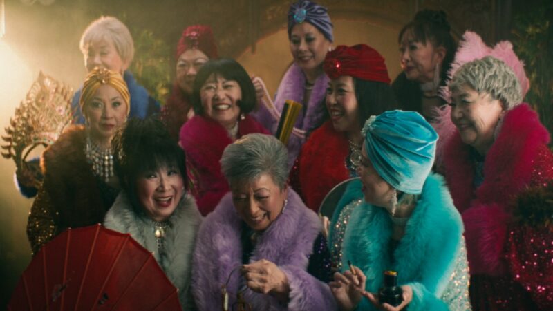 A group of older Asian women in a group, wearing elaborate costumes and smiling