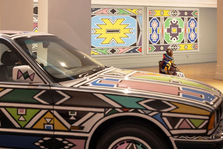 A car is covered in geometric designs in an art gallery.