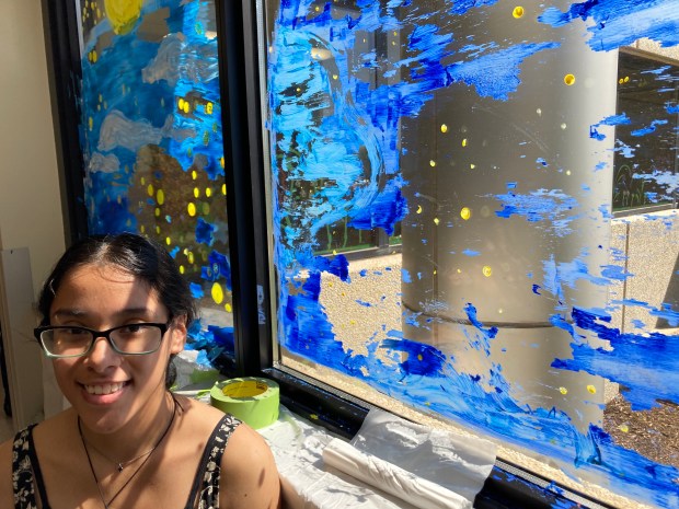 Faith Aparicio, a senior at Bremen High School in Midlothian, stands next to art she painted on a window Wednesday, May 1, at Advocate South Suburban Hospital in Hazel Crest. Some of the paint started flaking off of her original image, so she altered it and channeled famous painter Bob Ross, calling it a 