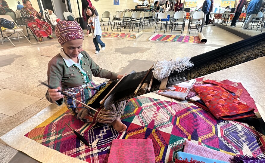 Evelynda Otong at her loom and Idiyanale Padrigan plays in the background.