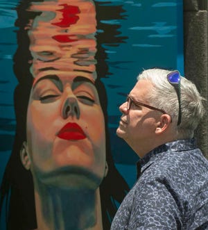 Mark Guidi of Tampa is juxtaposed by a painting by artist Pavlina Alea of Atlanta during the Mayfaire by-the Lake in Lakeland in 2021.