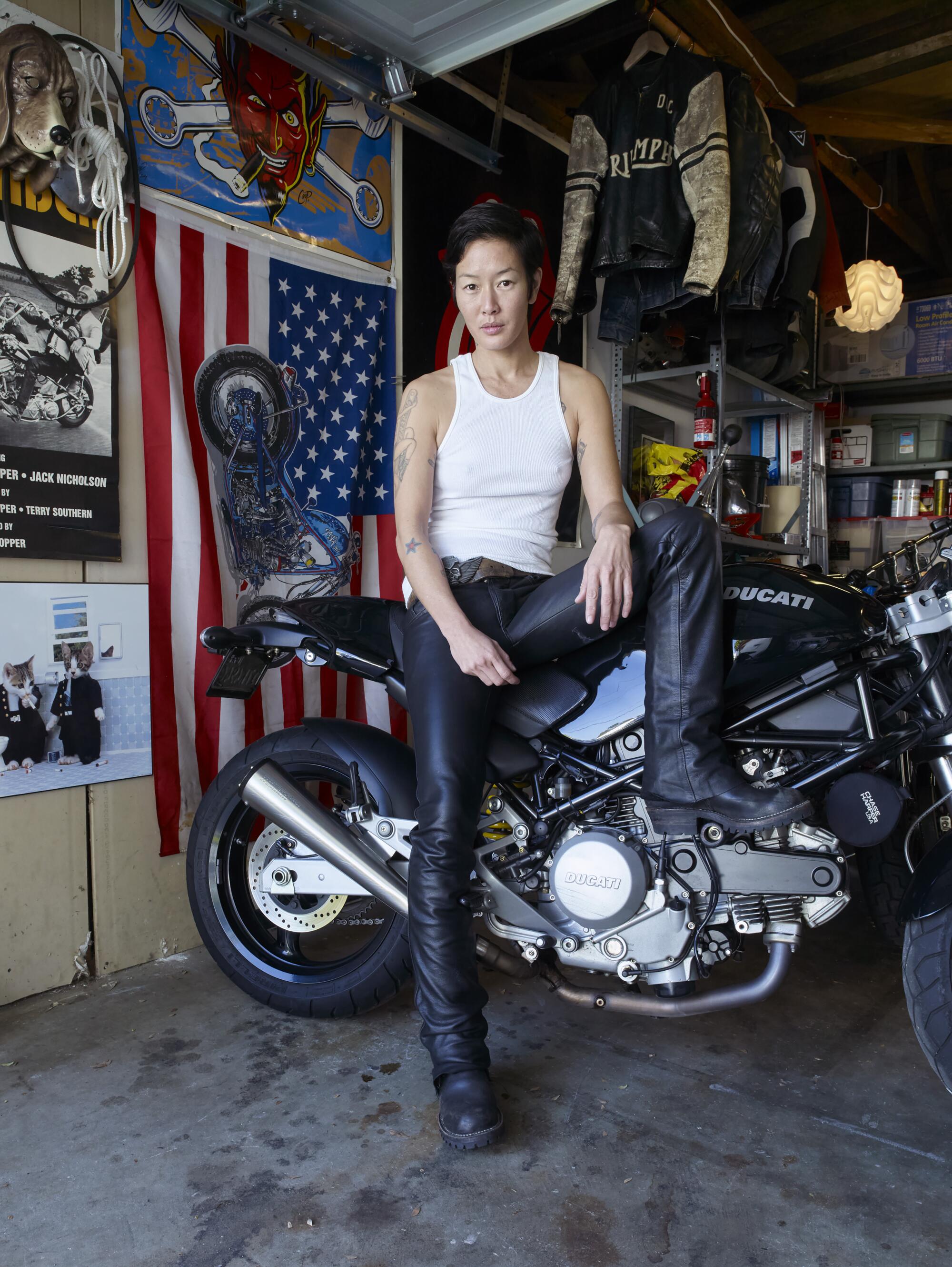 Image titled "Jenny Shimizu" shows a young woman wearing a tank top and jeans sitting on her motorcycle in a garage