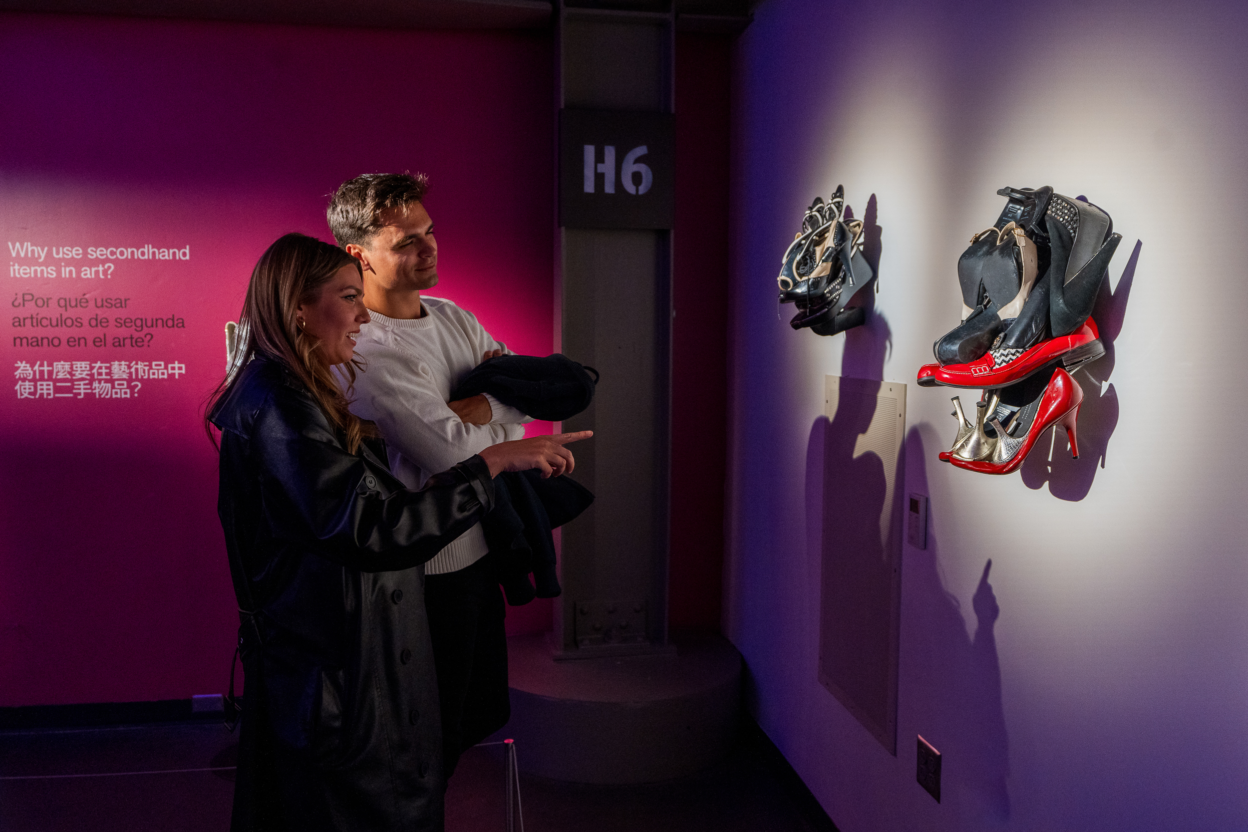 Two people stand in front of sculptures made of used shoes