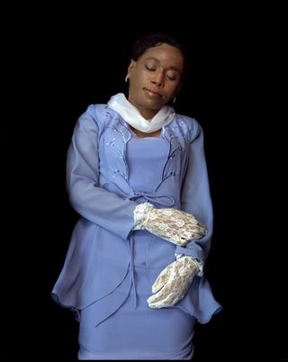 Photograph of Black woman in lilac suite and white gloves, at rest