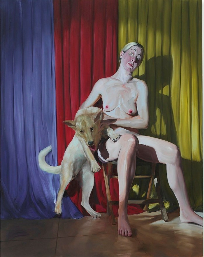 In a painting, a young blonde woman sits on a wooden chair on a theatre stage as the spotlight illuminates her naked figure against a purple, red and yellow curtain. She holds a dog with both her hands while looking to her right.