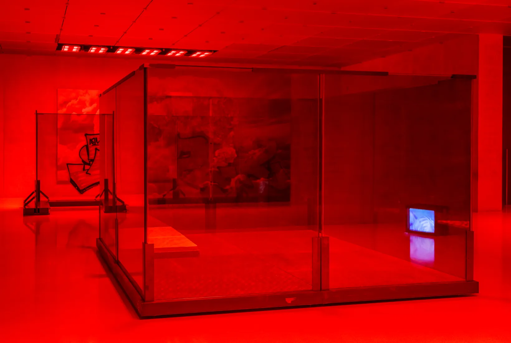 A red lit room in an art gallery where a large glass-walled structure stands